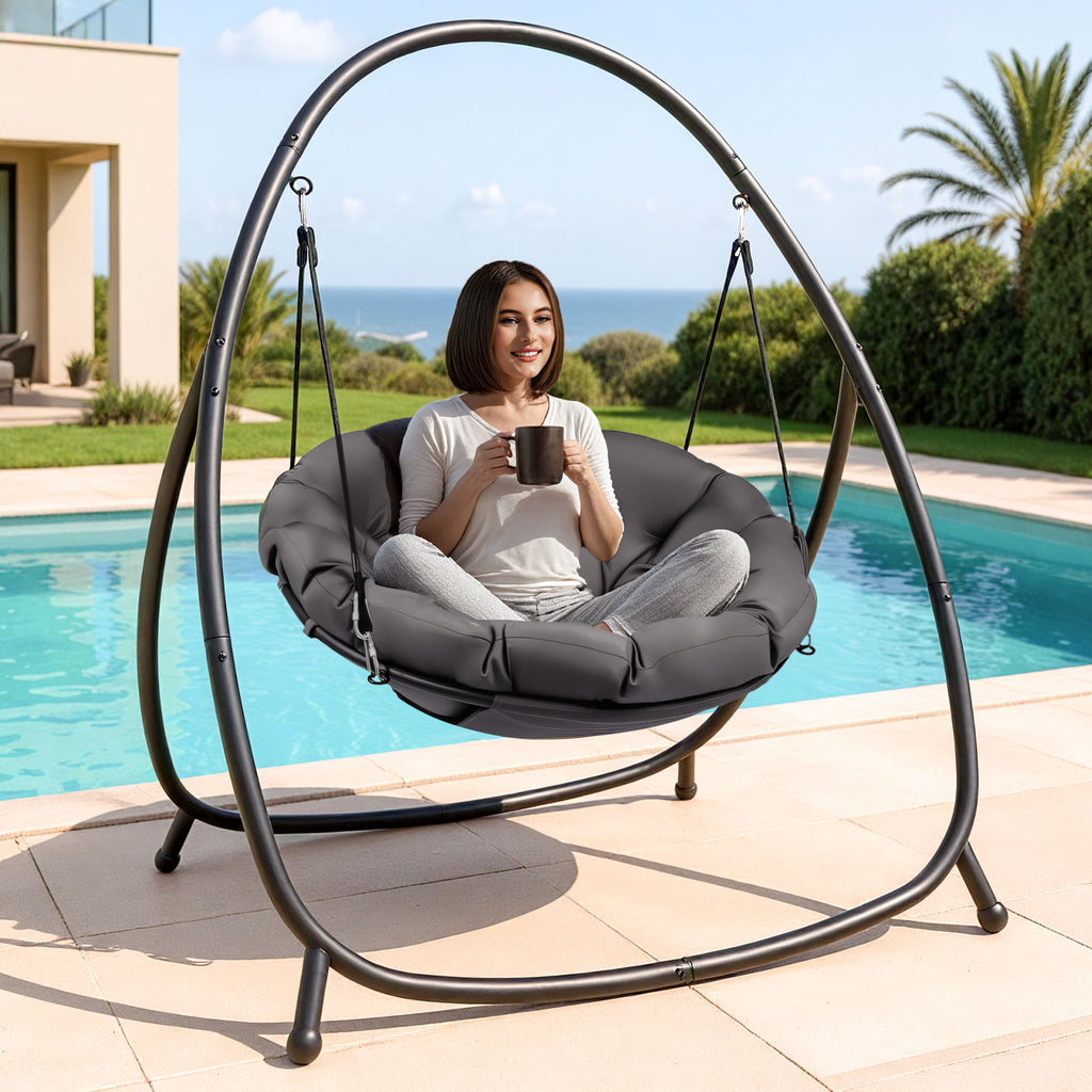 Woman sitting in a gray hanging chair by a pool with a scenic background
